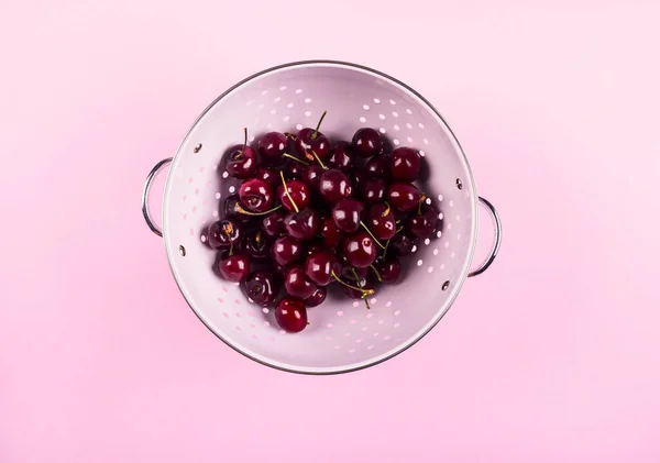 Heap of cherries in colander on pink background — Stock Photo, Image