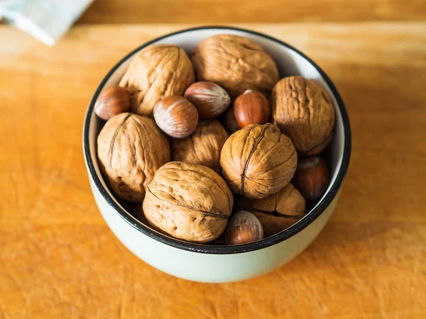 Walnuts and hazelnuts in bowl on wooden board. — Stock Photo, Image