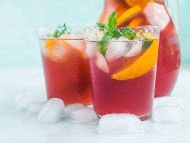 Sürahide taze kırmızı kokteyl mocktail sangria ve parlak turkuaz arka planda buzlu bardaklar, nane yaprakları ve limon ve portakal dilimleri. Yakın çekim.