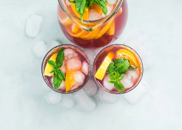 新鲜的红色鸡尾酒在水壶和玻璃杯与冰 薄荷叶和柠檬和橙片明亮的绿松石背景 顶部视图 — 图库照片