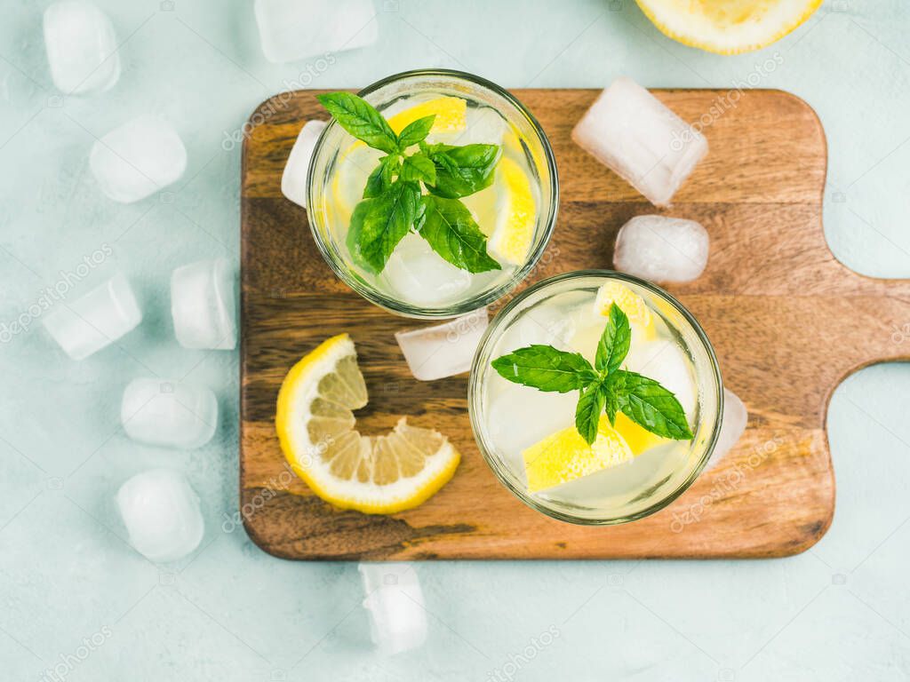 Fresh lemonade in jug and glasses with ice, mint leaves and lemon slices on bright gray and blue background. Top view