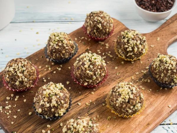 Home made vegan energy protein balls with oats, nuts, dates, dried fruit, flax and hemp seeds, chocolate nibs and maple syrup served in paper cases on wooden board.