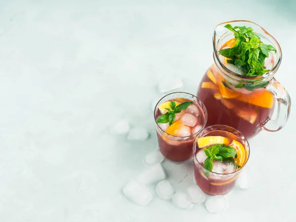 新鲜的红色鸡尾酒在水壶和玻璃杯与冰 薄荷叶和柠檬和橙片明亮的绿松石背景 顶部视图 — 图库照片