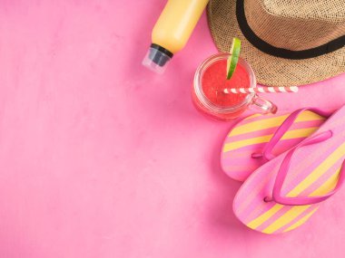Hasır şapka, renkli parmak arası terlik, sarı güneş koruyucu sprey ve pembe arka planda ferahlatıcı kırmızı karpuz smoothie. Yaz tatili, rahatla, kopyalama alanı