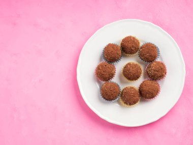 Ev yapımı, yulaflı, fındıklı, badem ezmeli, hurma, kurutulmuş meyve, keten tohumu, pembe ahşap zemin üzerinde çikolata parçacıkları bulunan vegan enerji topları. Üst görünüm, alanı kopyala
