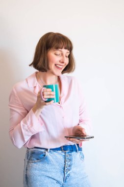 Kadın kahve içiyor ve akıllı telefon kullanıyor.