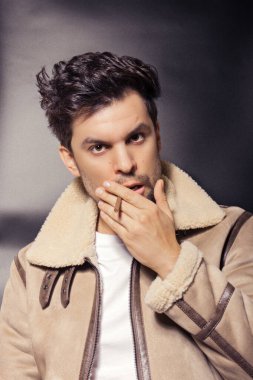 Koyun derisi ceketli bir adam ağzında bir sigara tutuyor ve objektife bakıyor.