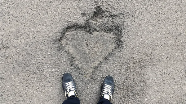 sign of the heart on the asphalt and feet in sneakers - top view