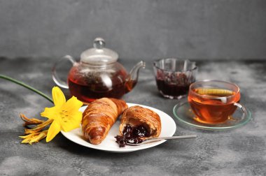 Kruvasan-çay, kruvasan, karanlık bir arka plan üzerinde Lily ile kahvaltı