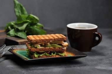 koyu arka plan ve kupa bir tabakta tavuk göğsü ile kare sandviç