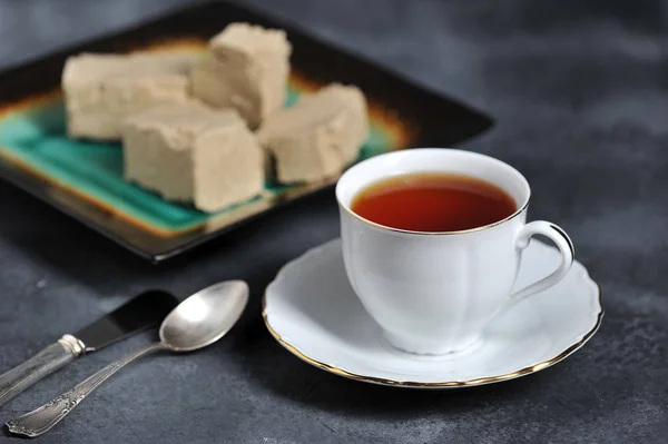 tea in a mug with a golden edge and a saucer and halva cut into pieces - oriental tea
