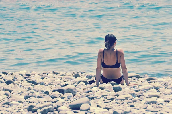 Menina Solitária Biquíni Boné Beisebol Sentado Uma Praia Pedra Olhando — Fotografia de Stock