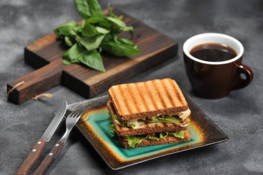 koyu arka plan ve kupa bir tabakta tavuk göğsü ile kare sandviç