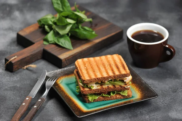 koyu arka plan ve kupa bir tabakta tavuk göğsü ile kare sandviç