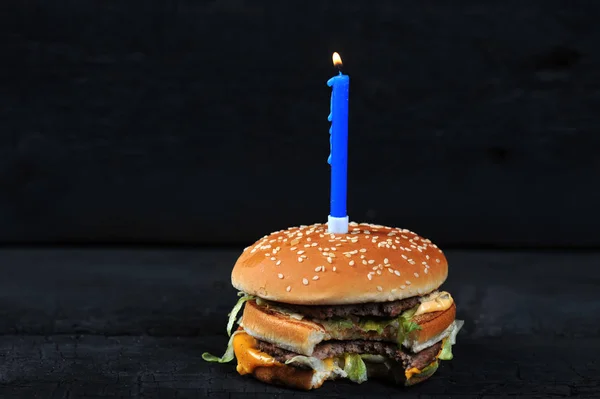 bitten burger with a candle with fire on a dark rustic background