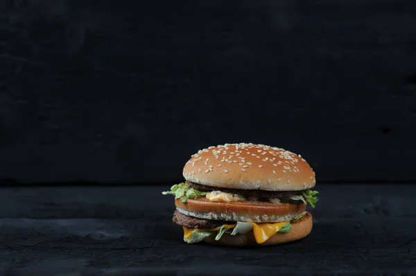 Burger with sesame bun on black background front view, copyspace