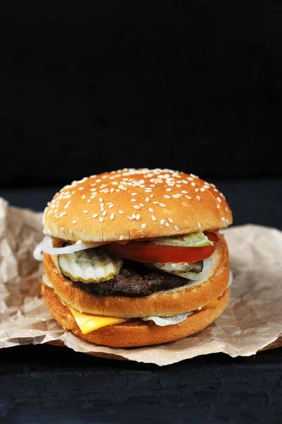 fast food-cut in half or bitten Burger with cheese and beef on Kraft paper on black charcoal background