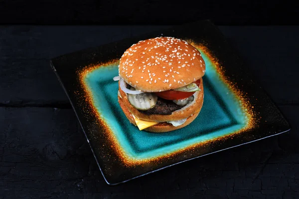 fast food Burger with cheese and beef on a plate on black coal background