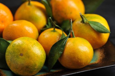 rustik bir siyah arka plan üzerine bir tabak içinde yapraklarla mandalina 