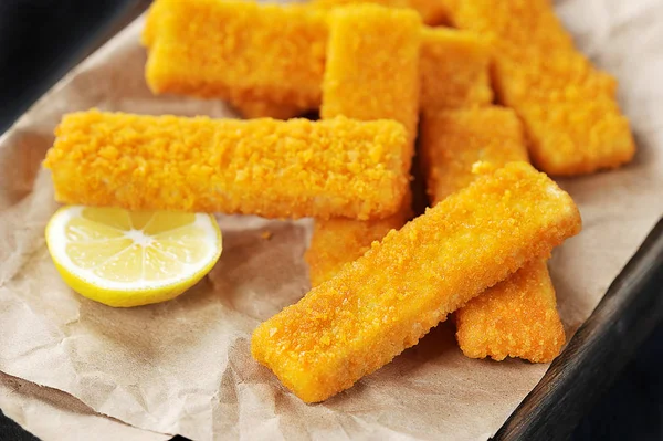 fried breaded fish sticks and lemon on paper - closeup