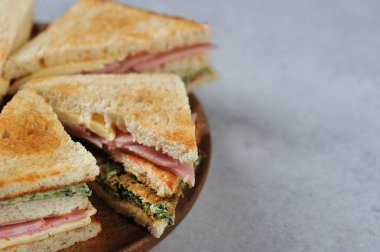 ahşap bir tabak üzerinde jambon ve peynirli sandviç