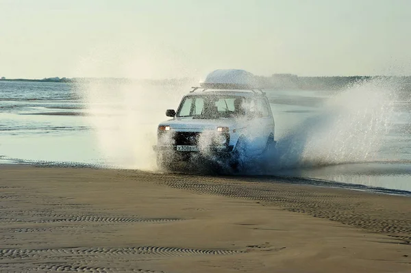 Carro russo Niva monta em uma estrada costeira com salpicos de unde — Fotografia de Stock