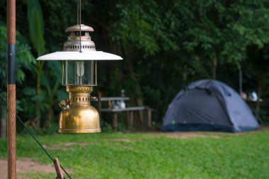 Ormandaki kamp alanındaki yeşil çimenlikteki çadırların bulanık arka planına sahip klasik kamp feneri.