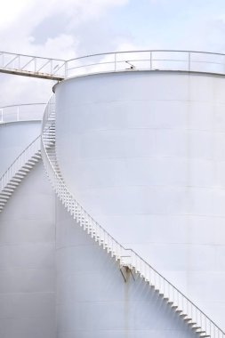Dikey çerçevedeki beyaz depolama tankları üzerindeki sarmal merdivenlerin düşük açılı görüntüsü