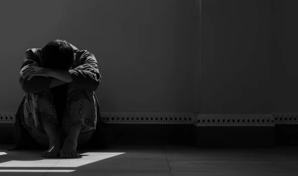 无望的男人独自坐着 双膝跪在地板上 在空荡荡的黑漆漆的房间里 阳光和阴影笼罩着他 — 图库照片