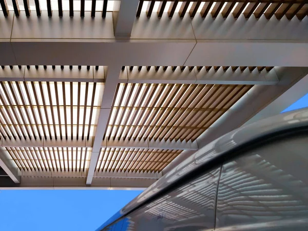 Ön planda arabanın bulanık parçasıyla binanın dışındaki modern çatı güneşliğinin düşük açılı görüntüsü