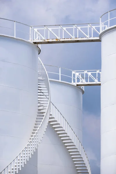 Low angle view of curve spiral staircase on white storage fuel tanks in vertical frame