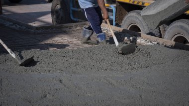 İnşaat alanındaki zemine beton serpmek için çapa kullanan Asyalı inşaat işçisinin kesilmiş görüntüsü.