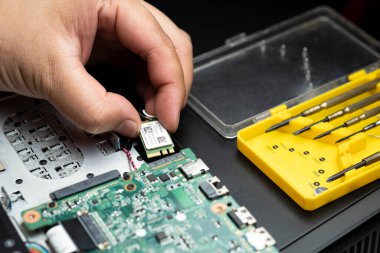 Bilgisayarın ana kartına yüklemek için elinde kablosuz kart tutan teknisyenin elindeki seçici odak siyah masa üstündeki sarı kutuda tornavidalar, bilgisayar onarım konsepti