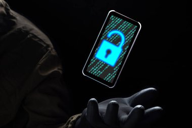 Kilit açma simgesini, bilgisayar korsanının elinde siyah bir eldiven, hackleme ve internet siber suç kavramının üzerinde yüzen akıllı telefon ekranında yeşil ikili kodla kapat