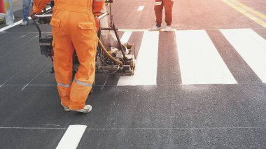 Şehirdeki asfalt yol yüzeyinde yaya geçidi boyamak için termoplastik sprey yol işaretleme makinesi kullanan yol işçilerinin düşük kesimi 