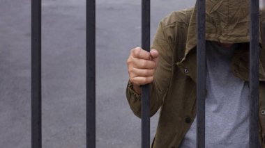 Umutsuzluğun bir parçası olarak kapüşonlu adam başını eğip demir çubuklar tutuyor, göçmen ve mülteci krizi umutsuz bir konsept içinde.