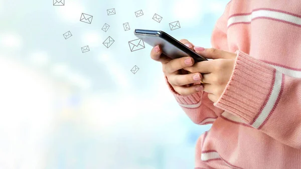 Pembe kazak giyen genç bayanı kapat. Akıllı telefon kullan. Mavi arka planda bulanık iç aydınlatma içeren e-postalar gönder.