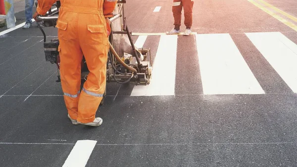 市内のアスファルト路面上の歩行者横断歩道を塗装するために熱可塑性スプレー道路マーキングマシンを使用して道路労働者の低セクション — ストック写真