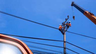 Vinci olan iki elektrikçinin düşük açılı görüntüsü mavi gökyüzü arka planına karşı elektrik direğine elektrik sistemi kurmaya çalışıyor