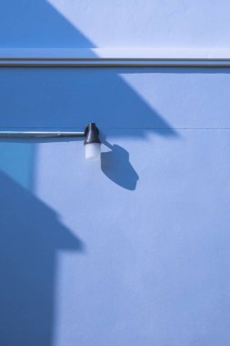 İki katlı evin mavi beton duvarında elektrik borusu olan duvar lambası. Güneş ışığı ve gölgesi dikey çerçeve ve minimalist tarzda.