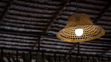 Geleneksel kulübede saman çatı döşemesine karşı bambu çiftçi şapkasıyla klasik asma lamba dekorasyonunun düşük açılı görüntüsü