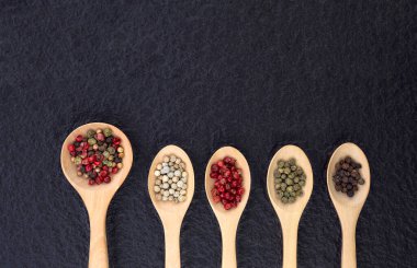 Tahta kaşıkta siyah taş kaplama arka planda çeşitli renklerde biberlerin olduğu düz bir yer.