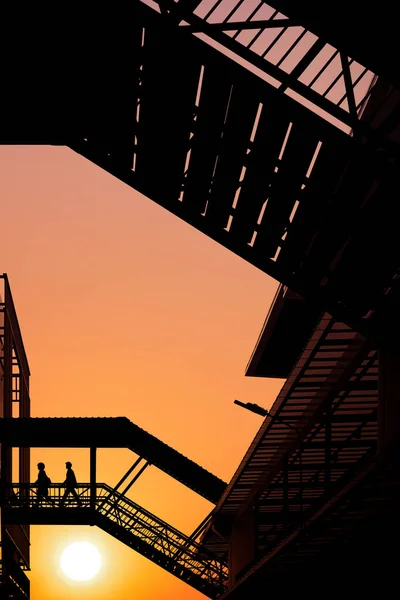 日落时分 工作人员在人行天桥上行走 在夕阳西下的天空背景下 低视角和垂直框架下将建筑物连接起来 — 图库照片