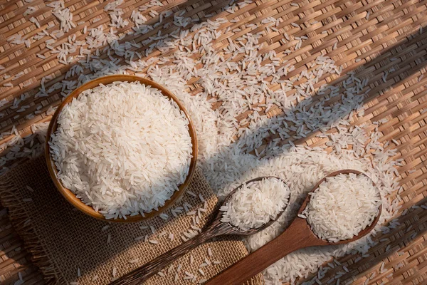 Seramik kasede, harman sepetinde tahta kaşıklarla beyaz pirinç (Tayland Jasmine Rice) yüzeyinde güneş ışığı ve gölge.