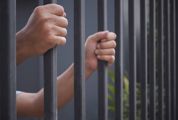 Side view and selective focus at right man's hand holding iron bars, dramatic border fence or prison with immigrant and refugee crisis, hope to be free concept