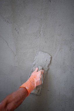Mason 'ın eli kauçuk eldivenle beton duvarın arka planına beton yapıştırmak için mala kullanıyor.