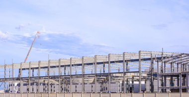 Vinç kamyonlu büyük fabrika sanayi iskeletinin metal yapısı, mavi gökyüzü arkaplanına karşı inşaat alanında çalışıyor.