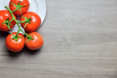 Dal üzerinde kırmızı domatesler, yuvarlak ahşap bir masada beyaz bir tabakta
