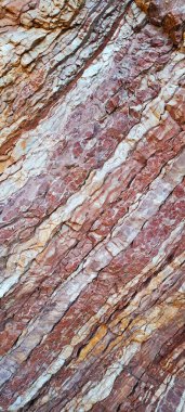 Katmanlı kaya oluşumlarının yakın görüntüsü kırmızı, turuncu ve beyaz tonlardaki doğal çizgileri, jeolojik desenleri ve engebeli yüzey detaylarını gösteriyor..