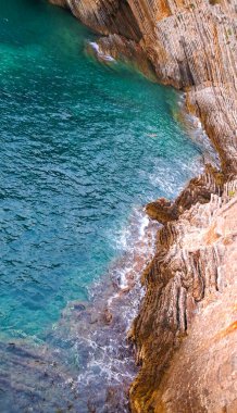 Sarp bir kıyı şeridindeki engebeli kaya oluşumlarına karşı turkuaz deniz suyu turkuazları çarpıcı jeolojik dokuları ve karayla denizin dinamik buluşmasını gözler önüne seriyor..